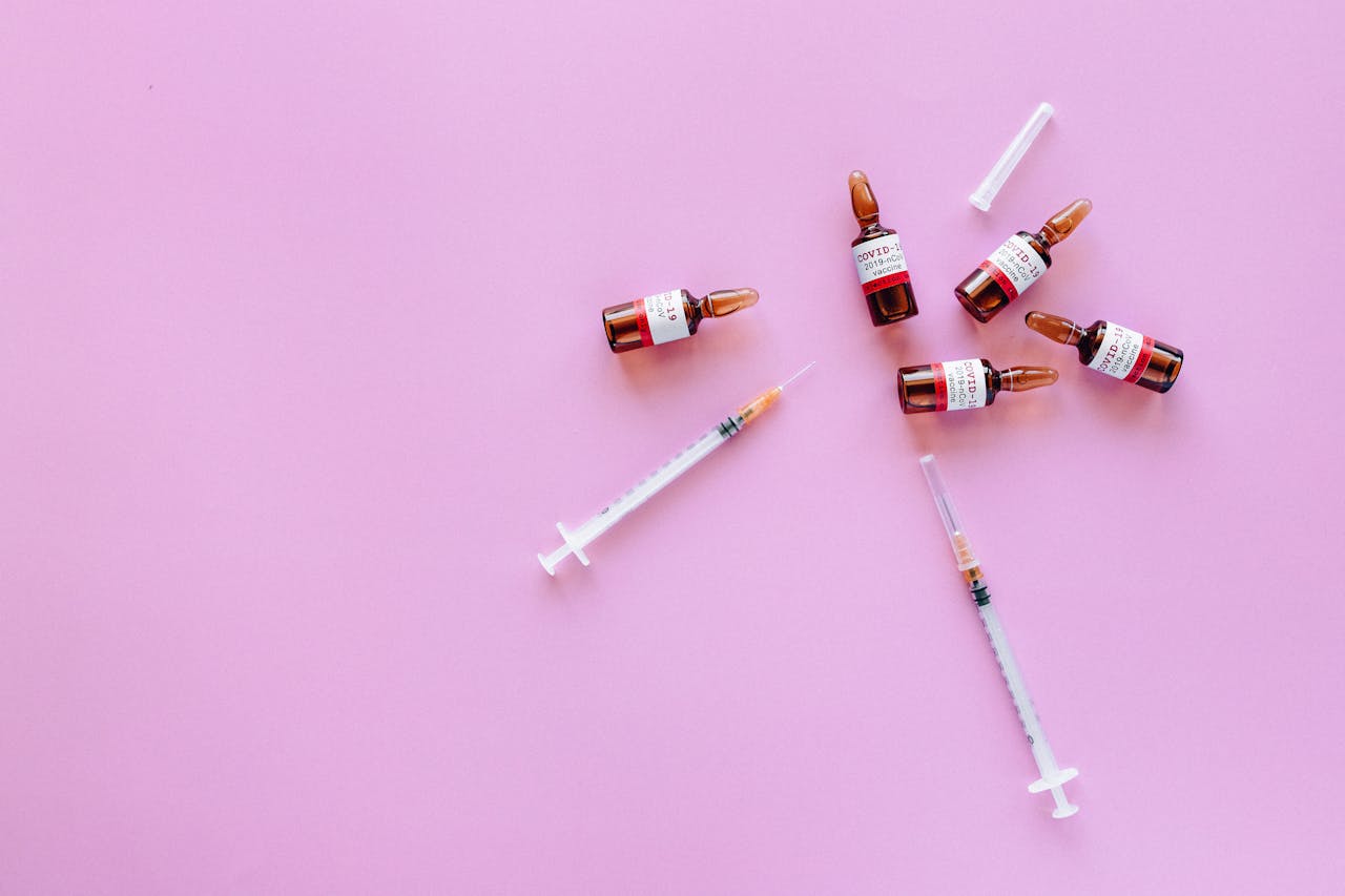 Vaccine vials and syringes displayed on a pink background, symbolizing healthcare and immunization.